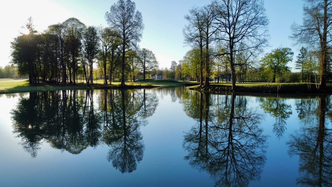 Vue aérienne du parcours du Golf International Clément Ader au petit matin, plans d'eau et arbres reflétés